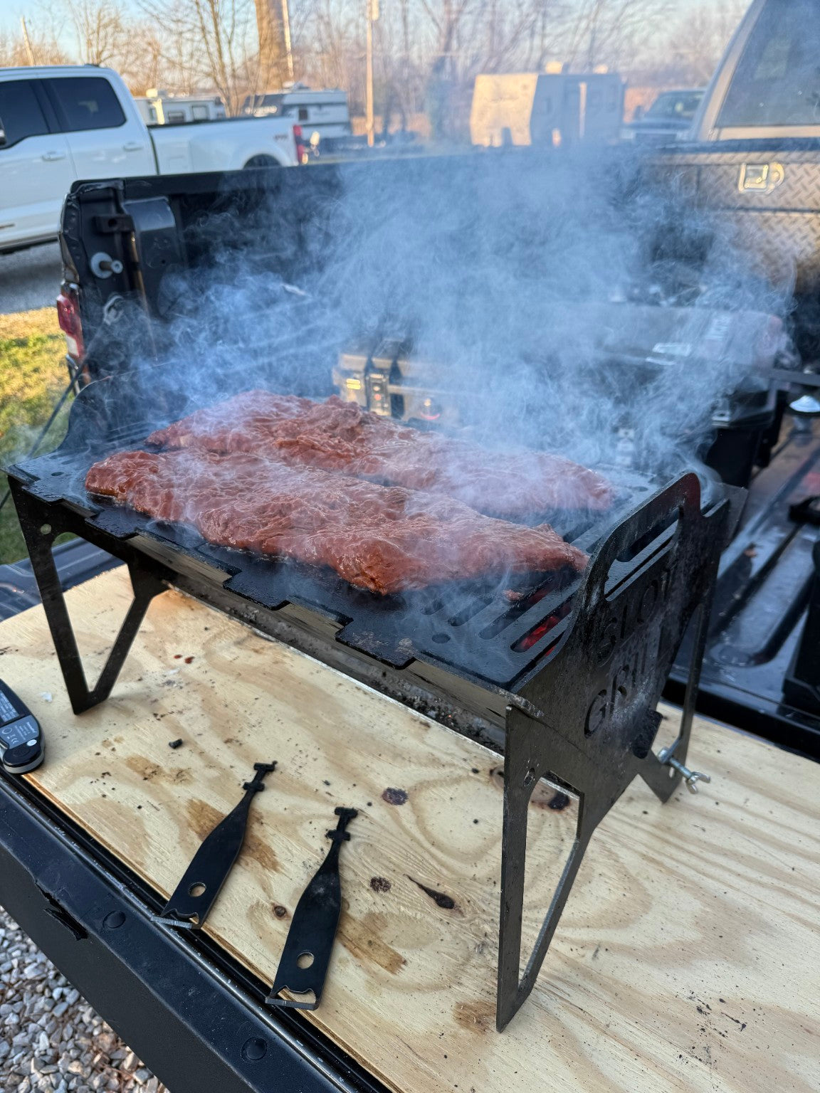 Customer cooking steaks on a Slot Grill flat-pack charcoal grill on a pickup tailgate