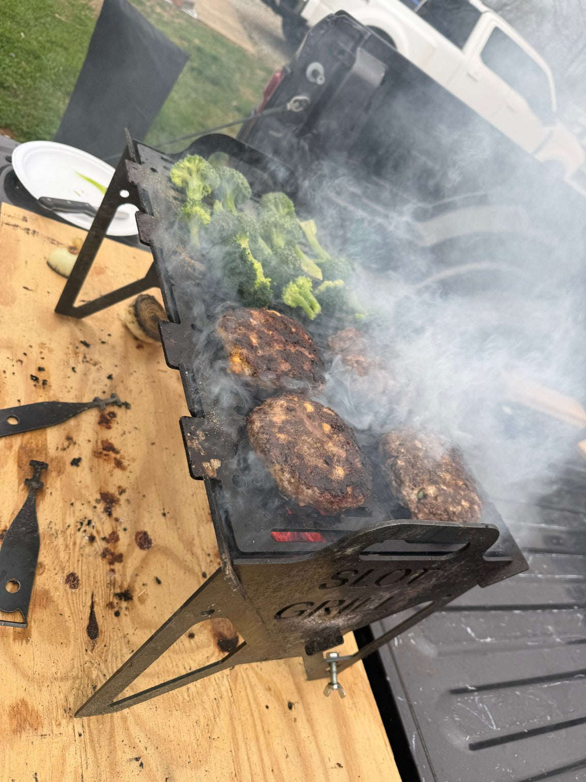 Customer photo of burgers and broccoli cooking on a Slot Grill flat-pack charcoal grill