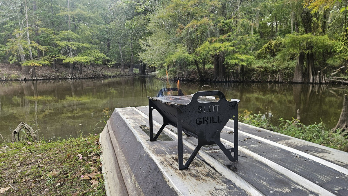 Slot Grill portable charcoal grill with flames beside a cypress bayou in Southeast Texas