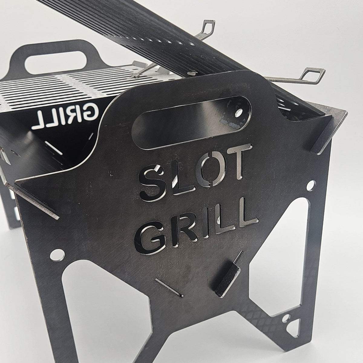 Close-up of the laser-cut Slot Grill logo on a thick carbon steel side panel