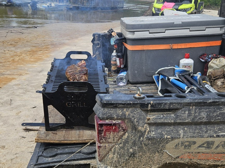 Slot Grill cooking from the rear of a muddy side-by-side beside the water