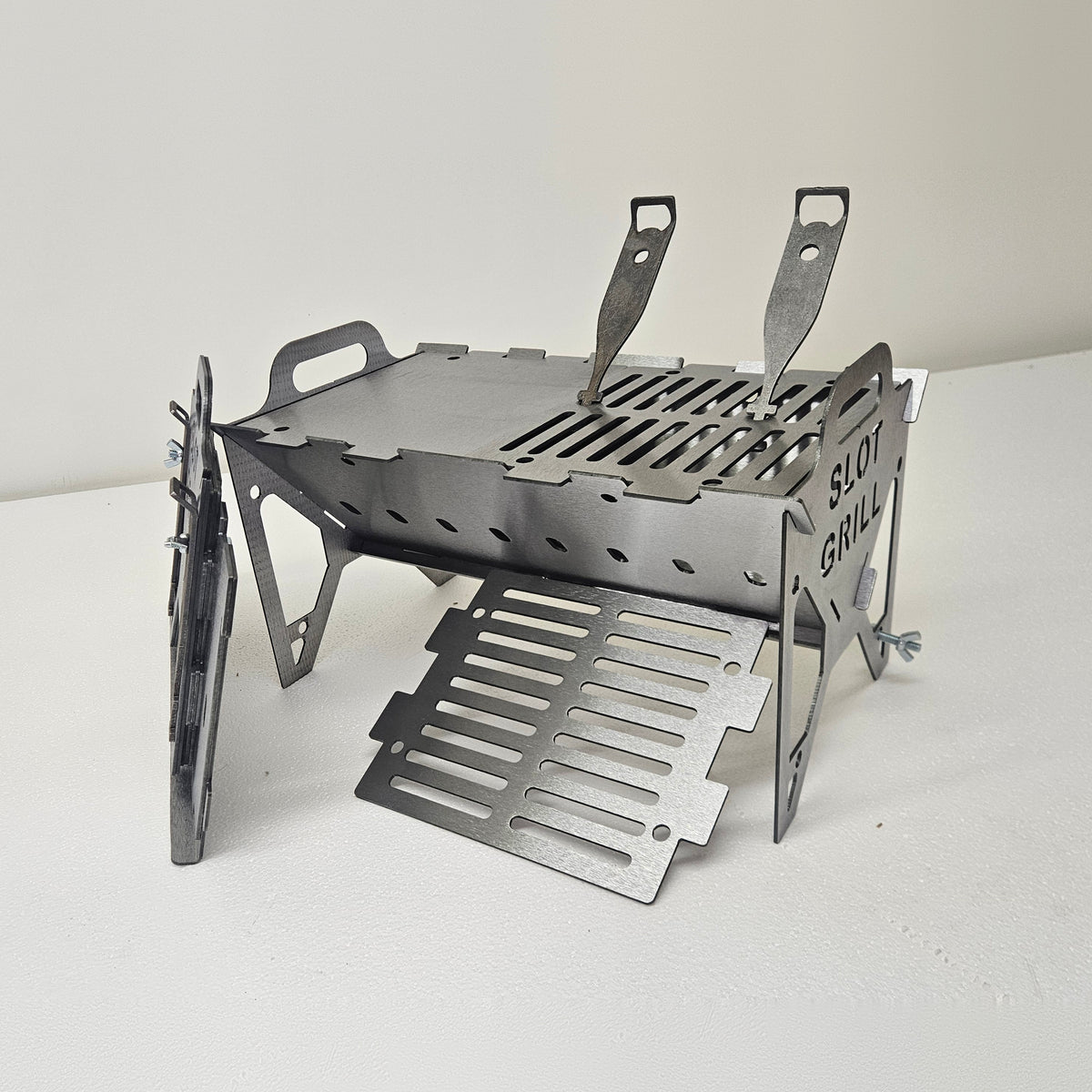 Slot Grill Compact with a solid griddle plate on one half and a slotted grate on the other, spare grate in front